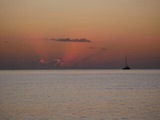 A breathtaking sunset over the calm sea with a sailboat on the horizon. Warm orange and golden...