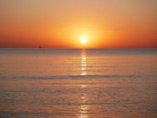 Vivid sunset over the sea with a glowing sun and golden reflection on the calm water. Peaceful and captivating atmosphere. Nature background, relaxation concept, travel theme and inspirational visual