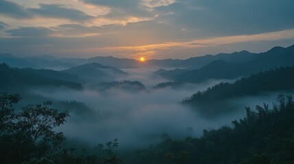 A breathtaking sunrise paints the sky orange and yellow as it rises above a misty valley nestled between rolling, dark green hills