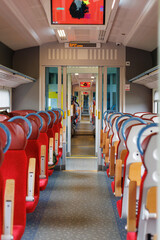 Perspective view of a clean and empty train corridor with red seats and modern design.