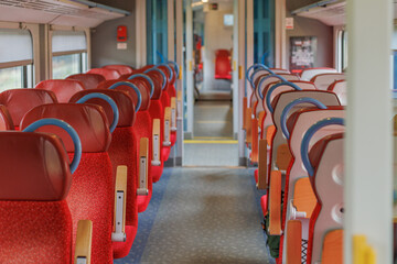 Empty train carriage with an aisle and rows of red chairs on both sides.