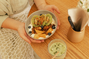 Close-up of female hands holding a plate. Granola with fresh fruit and yoghurt. A healthy natural breakfast in a ceramic plate on a wooden kitchen table
