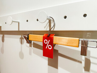 Wooden hanger with a red sale tag, showing a percentage discount. A wooden clothes hanger with a...