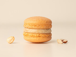Nut macaron with cream filling and nut pieces on beige background