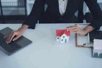 Real Estate Deal: A professional in a business suit interacts with a miniature house and a laptop,...