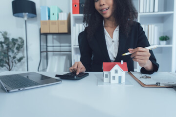 Real Estate Agent Consultation: A friendly real estate agent sits at her desk, using a calculator...