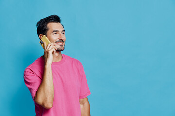 Smiling man wearing pink shirt talking on mobile phone, looking cheerful and happy against a bright...