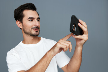 Young man smiling while using a mobile phone, casually dressed in white t-shirt, against a solid...