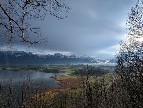 Beautiful panoramic landscape of snow-capped mountains reflected in lake water, spring season alpine scenery, dramatic cloudy sky and nature travel destination.