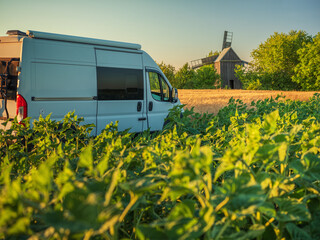 white van in field of sunflower and wheat with view to old wooden mill