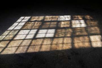 Soft natural light casting grid window shadow on aged concrete floor, ideal for use as graphic...
