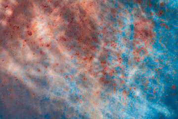 Macro of rust spots on weathered blue painted metal, forming an abstract textured pattern with...
