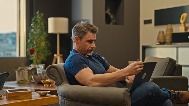 Casual mid adult man with laptop computer in home office, banking online, remote working. Portrait of older bearded guy thinking. Businessman, entrepreneur managing business on internet.