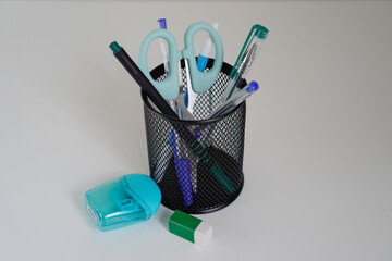 Office supplies in the pencil holder on the white table, light background, blue colors