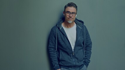 Obraz premium Middle aged man wearing glasses standing confidently with a relaxed smile by a gray background. Portrait of happy mid adult male in 50s, bearded, grey hair, smiling.