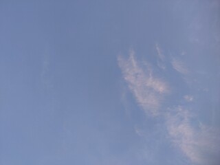 A calm sky at dusk with scattered clouds and a soft moon glowing in the serene blue horizon.