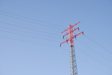 Roter Strommast mit Hochspannungsleitungen vor klarem blauen Himmel