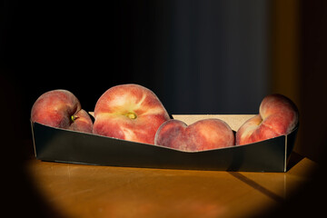 Sunlit Flat Peaches in a Tray on Dark Background