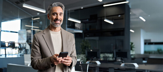 Happy mature older business man wearing suit using mobile cell phone at work. Middle aged...