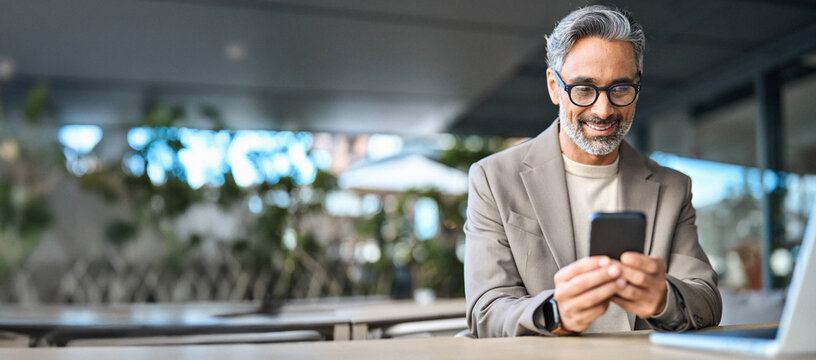 Happy stylish older busy businessman investor holding smartphone looking at cellphone doing banking payments. Middle aged business man using mobile cell phone working outdoors. Candid photo.