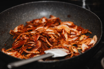Sliced onion with paprika powder in a pan, fried on a gas stove, with a visible spatula, in natural light