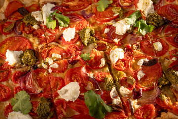 Close up of a sliced homemade pizza with tomatoes, ricotta, pesto and coriander, displaying vibrant colors and textures