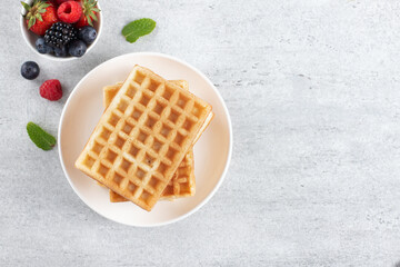 Stack of crispy plain Belgian waffles with berries on a gray background. Top view. Copy space.