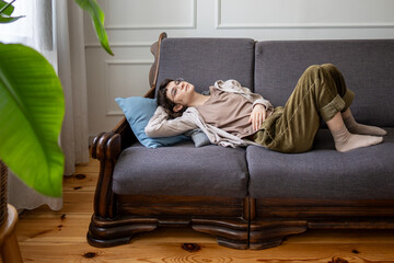 Dreamy lazy woman lounging on sofa at home alone, lost in thoughts with indifferent mood. Idleness,...