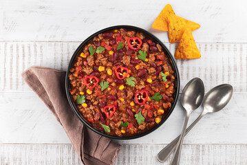 Bowl of meat mexican spicy stew with beans and corn chili con carne on white wooden background.