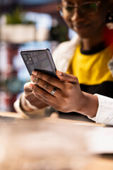 Focus on smartphone used by happy african american woman playing videogames, enjoying leisure time at home. Close up of cheerful gamer enjoying game on mobile phone, having fun in apartment