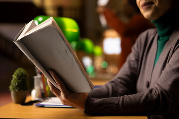 Focused adult woman with a book in hand studying in a quiet library space, working hard to graduate...