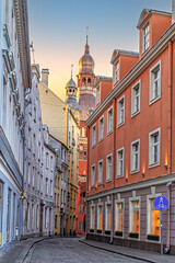 Obraz premium Riga, Latvia. Narrow cobblestone street in the Old Town, lined with colorful historic buildings, leading to a tall clock tower, capturing the charm of urban architecture and historical ambiance