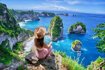 Fotobehang Bali Woman traveler sitting on rock cliff and enjoying of scenic amazing landscape of Diamond beach during vacation to Nusa Penida Island in Indonesia, travel to touristic beautiful destinations  © Goffkein