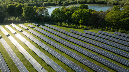 An expansive solar panel farm nestles in the green, serene landscape by a sparkling lake.