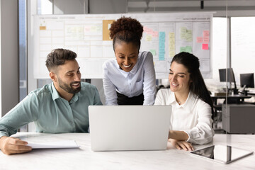 Three cheerful creative professionals, marketing department members gathered in office working...