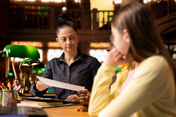 Woman teacher helping students prepare for an exam by providing materials for learning, fostering...