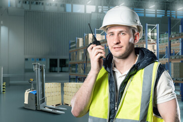 Warehouse worker in safety vest and helmet using walkie-talkie near stacked boxes and pallet truck....