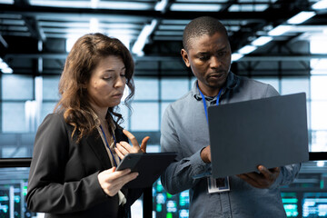 Programmers in data center using laptop and tablet, executing security patches, securing firewall....