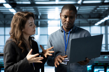 Computer scientists using laptop in data center, managing server virtualization. Teamworking server...