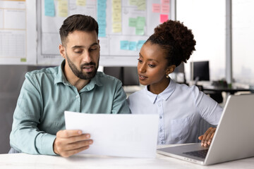 Two colleagues reviewing document together at desk in modern office, analyzing written information, discussing content of legal document, collaborating on joint task while carefully examining paper
