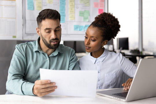 Two colleagues reviewing document together at desk in modern office, analyzing written information, discussing content of legal document, collaborating on joint task while carefully examining paper