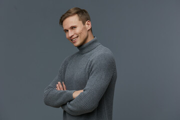 Smiling young man with short hair wearing cozy gray turtleneck sweater looking confidently at...