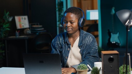 Cheerful woman relaxing at home by watching TV show on laptop using headphones. Happy person...