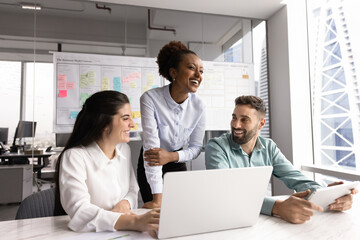 Group of three teammates engaged in positive communication in workplace using laptop and modern...