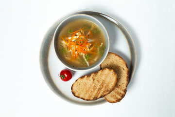 A bowl of chicken soup with vegetables and toast on a white background