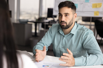 Professional man explains information presented in charts on table, outlining next steps of...