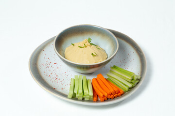 Plate of hummus with fresh vegetables — carrot, celery, and cucumber sticks — on a white background