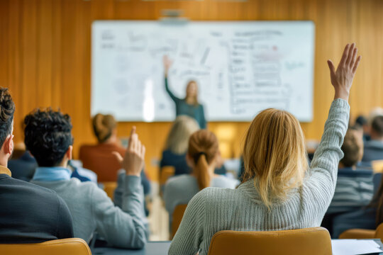 Engaged participants raising their hands during a business seminar or training session, with a blurred presenter writing on a whiteboard in the background.