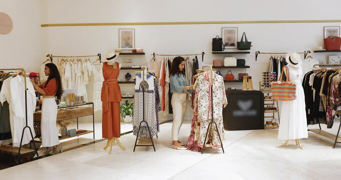 Diverse female customers choosing stylish branded clothes in fashion store showroom, sorting goods hanging on rack, enjoying shopping in sales area. Shop assistants checking prices