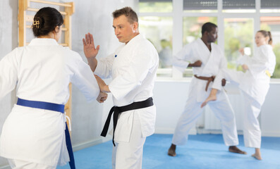 Adult man and young woman in kimono train judo techniques in group in studio